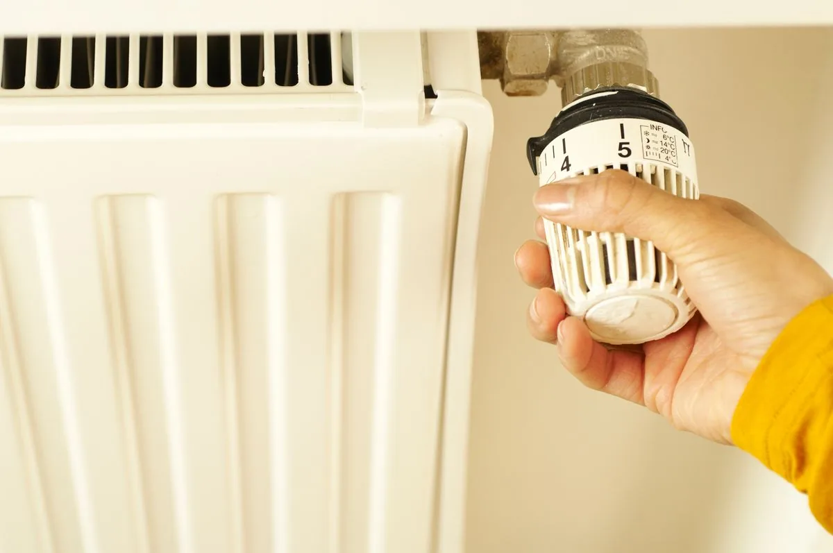 A hand turning down a radiator valve at home